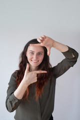 Cheerful pretty Caucasian girl showing photo sign and smiling. Young female photographer ready for work. Right perspective concept