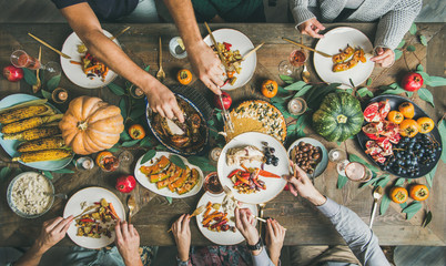 Traditional Thanksgiving or Friendsgiving holiday celebration party. Flat-lay of friends feasting at Thanksgiving Day table with turkey, pumpkin pie, roasted seasonal vegetables and fruit, top view