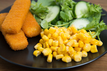 Fish fingers with green salad and corn. Healthy food for kids.