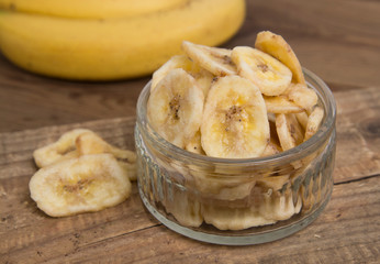 Banana chips inglass bowl, close up view. Rustic wooden board. Healthy dried fruits.