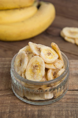 Banana chips inglass bowl, close up view. Rustic wooden board. Healthy dried fruits.