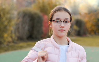 Close-up portrait of beautiful preteen girl in fashion glasses with serious face expression outside...
