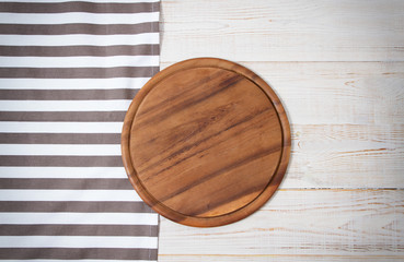 Round pizza cutting board and striped tablecloth on white wooden background. Top view. Copy space and mock up.