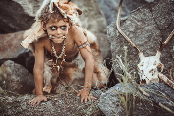 Fototapeta na wymiar Caveman, manly boy hunting outdoors. Prehistoric tribal boy outdoors on nature. Young shaggy and dirty savage, warrior and hunter hiding in an ambush behind a stone. Primitive ice age man in animal