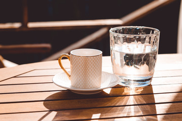 A cup of Turkish coffee and a glass of water on the wooden table on a terrace in a garden, coffee break, workplace, sunny day, chilling time
