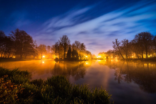 Park in Pszczyna, Poland on a starry night with gentle clouds and stars visible.