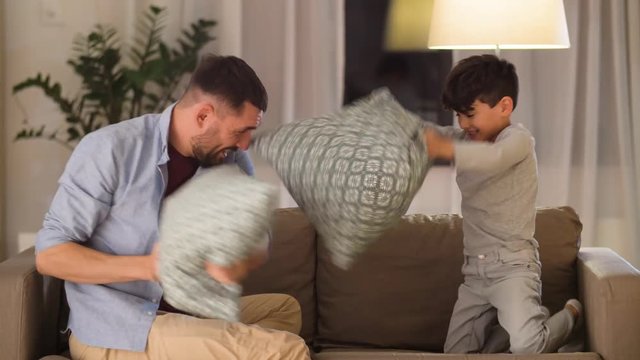 family, childhood and fatherhood concept - happy father and little son fighting by pillows having fun on sofa at home
