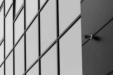 Black and white shot of Glass facade of modern office building with security camera and reflected clouds