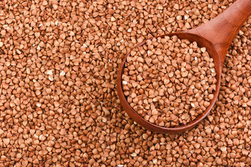 A wooden spoon full of buckwheat among the buckwheat. Top view
