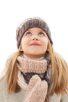 Beautiful little girl in cap and scarf looking up. Winter style. Isolated on white background

