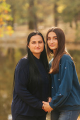 Mother with ldedt daughter stand in front of lake in the park. Yellow tree in autumn time