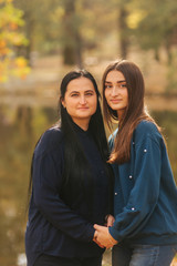 Fototapeta premium Mother with ldedt daughter stand in front of lake in the park. Yellow tree in autumn time