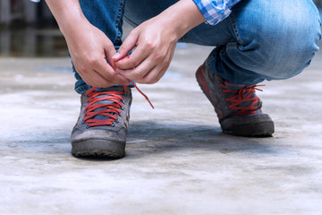 Hands of young man tying red shoelaces casual shoes on floor.