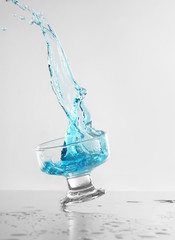 Glass of blue wine with splashes on white background