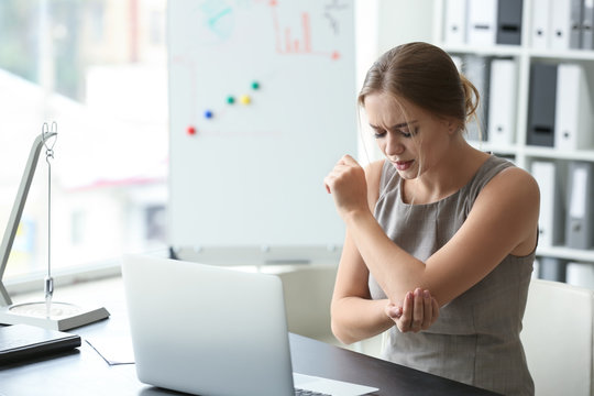 Young woman suffering from pain in elbow at workplace