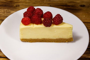 Piece of tasty New York cheesecake with raspberries in a white plate on wooden table