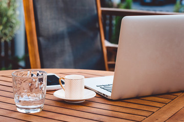 Laptop, a glass of coffee and a glass of water on a wooden table on a terrace, a place for business work outside and productivity 