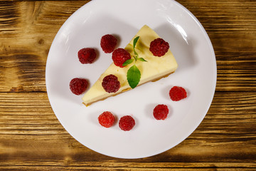 Piece of tasty New York cheesecake with raspberries in a white plate on wooden table. Top view