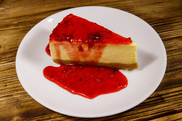 Piece of tasty New York cheesecake with raspberry jam in a white plate on wooden table