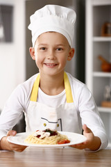 Cute little chef with tasty dish in kitchen