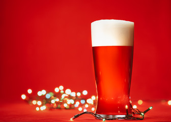 Pale ale or beer in pint glass with christmas lights on red background
