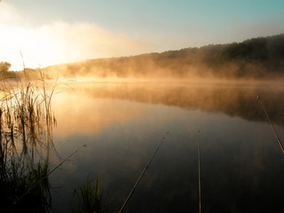 Beautiful red sunrise over the lake with fog and fishing rods