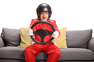 Mature man in a racing suit seated on a sofa holding a steering wheel © Ljupco Smokovski