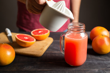 Freshly squeezed grapefruit juice is poured from a manual juicer in a jar with a handle.