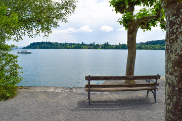 mainau island view through trees over lake constance, Bodensee, bench front of lake blue sky and...