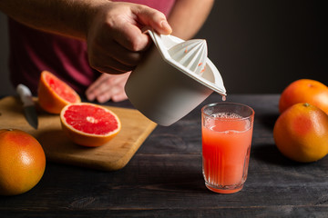 Freshly squeezed grapefruit juice is poured from a manual juicer in a glass.