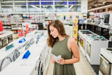 Woman buys washing machine in a store, holding manual. - obrazy, fototapety, plakaty