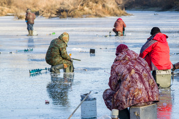 a group of people sitting on the first ice for fishing