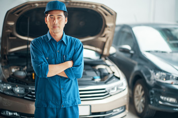Portrait of Asian maintenance worker standing in uniform with arms crossed in auto repair shop
