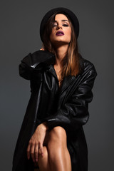 Young woman in black leather jacket and hat sitting in studio