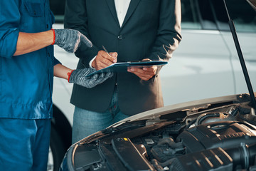 Close-up of auto technician in gloves pointing his client where he should to sign before repairing...