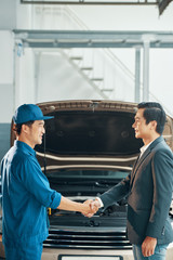 Auto mechanic shaking hands with car owner after repaired the car in auto salon