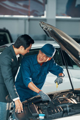 Fototapeta na wymiar Smiling Asian worker in uniform fixing the car and explaining the operation of the engine to the client in car service