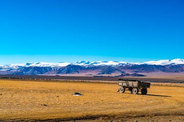 Obraz premium View of beautiful mountain range against the blue sky and the large yellow steppe with a herd of sheep grazing and a trailer loaded with ore near Ulgii in Mongolia