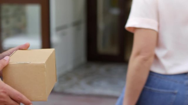 Mid-section close up shot of unrecognizable female customer giving cardboard box for shipping to male courier and walking away