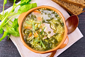 Soup with couscous and spinach in clay bowl on board top