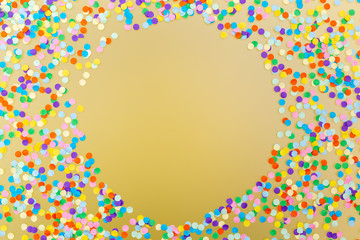Round frame of colorful confetti on yellow background.