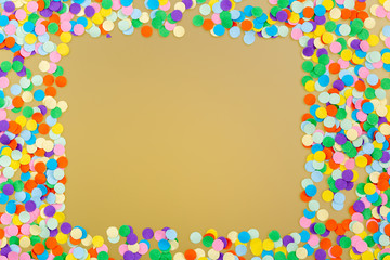Frame of colorful confetti on yellow background.