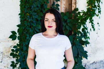 Attractive girl with black hair, on a background a white wall overgrown with wild grapes. Female sexuality. Be yourself.