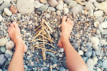 New Year tree from dry sticks and female legs on the sea pebble beach. Conceptual image of a New Year tree. Festive cheerful background