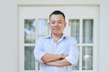 Portrait of confident Asian man with arms crossed standing outdoors near the house