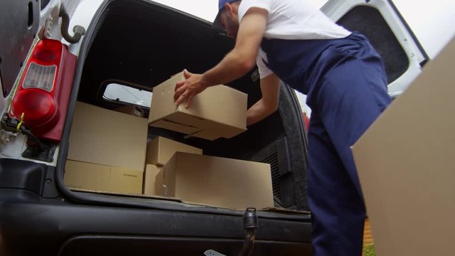 Low angle of male courier in uniform loading cardboard boxes into white delivery van