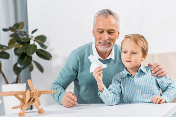 middle aged man and grandson having fun with paper plane at home