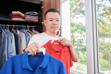 Young Asian man choosing casual style shirt or T-shirt in closet for dressing up in bedroom