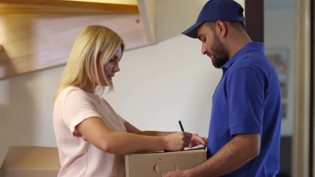 Medium shot of male bearded courier delivering packages to female customer and waiting as she is signing receipt on clipboard