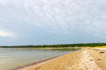 The sandy sea shore with the beach, the cloudy sky and the village at the distance. Taganrog bay, Azov sea, Russia